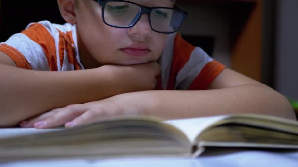 Inquisitivo, un chico serio con gafas está leyendo un libro interesante en casa — Vídeos de Stock