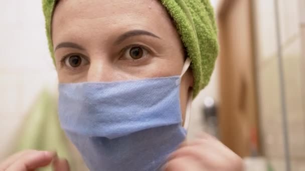 Jeune femme avec serviette verte sur la tête met masque sur le visage devant miroir dans le bain — Video
