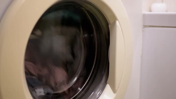 Waskleurige kleding in de huishoudelijke wasmachine. Een close-up. Draaiende trommel — Stockvideo