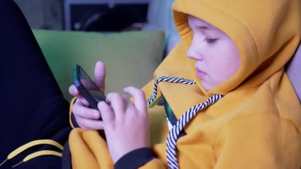 黄色胡迪男孩坐在沙发上，看着留言，在家里玩智能手机 — 图库视频影像
