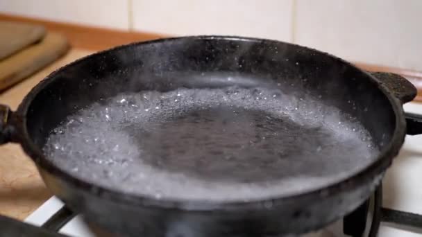 Verter agua de vidrio en una sartén caliente y grasosa. Líquido hirviendo, evaporación — Vídeo de stock