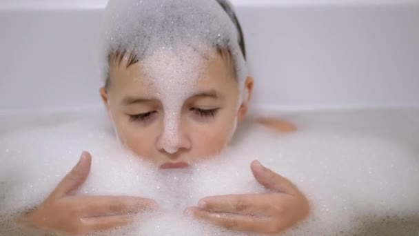 Junge badet im Badezimmer, spielt mit Seifenblasen, macht lustige Schaummasken — Stockvideo