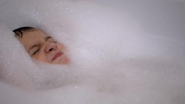 笑着躺在泡泡浴里的小男孩的脸。在水里放松。2.特写 — 图库视频影像