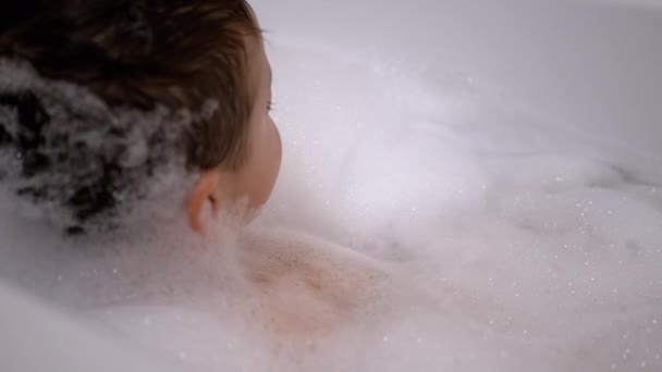 Mosolygó kisfiú fekszik a habfürdőben. Pihenés vízben. Közelkép — Stock videók