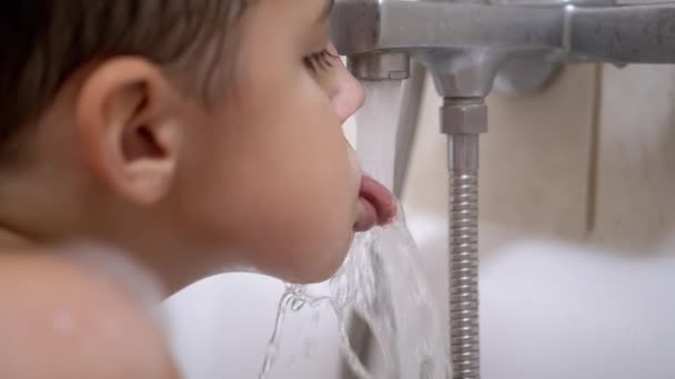 Menino sabe beber água da torneira com língua na casa de banho. Splashes fortes — Vídeo de Stock