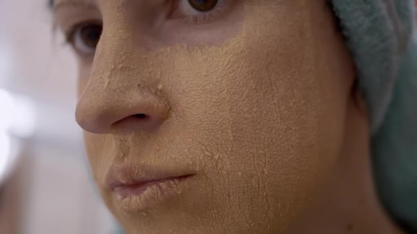 Goldene Kosmetikmaske auf dem Gesicht eines jungen Mädchens mit blauem Handtuch auf dem Kopf — Stockvideo