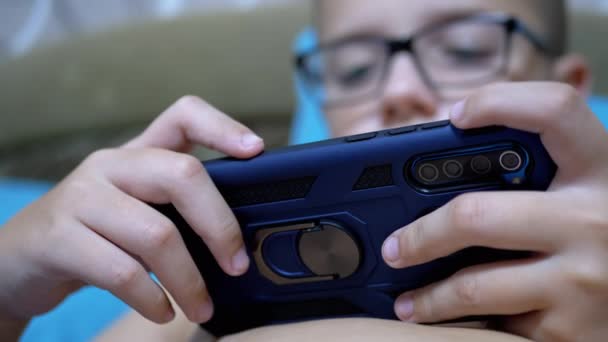 Σοβαρό Αγόρι με Γυαλιά Παίζει Κινητό Παιχνίδι Στο Smartphone Σε Χαλαρωμένη Κατάσταση Στο Κρεβάτι — Αρχείο Βίντεο