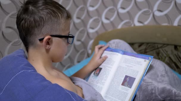 Serious Boy with Glasses is Reading an Interesting Book at Sit on Bed in Blanket — Stock Video