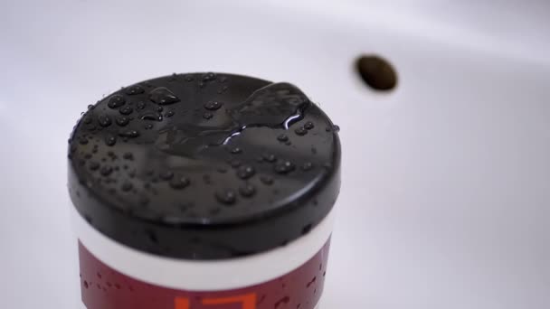 Gotas de agua caen lentamente del grifo y pulverizan sobre la superficie negra de la cubierta de plástico — Vídeos de Stock