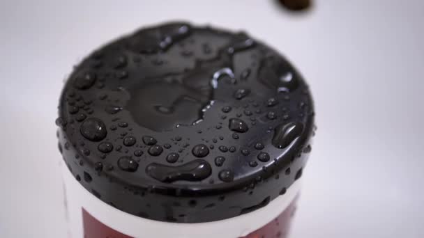 Des gouttes d'eau tombent lentement du robinet et pulvérisent sur la surface noire du couvercle en plastique — Video