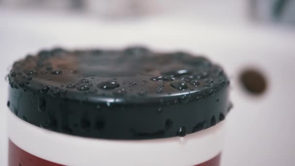 Капли воды медленно падают с крана и брызг на черную поверхность пластиковой оболочки — стоковое видео