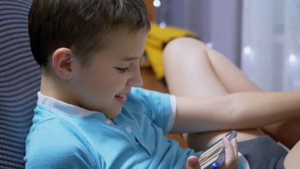 Glimlachende jongen Video kijken op een mobiele telefoon, zitten in stoel thuis. Close-up — Stockvideo