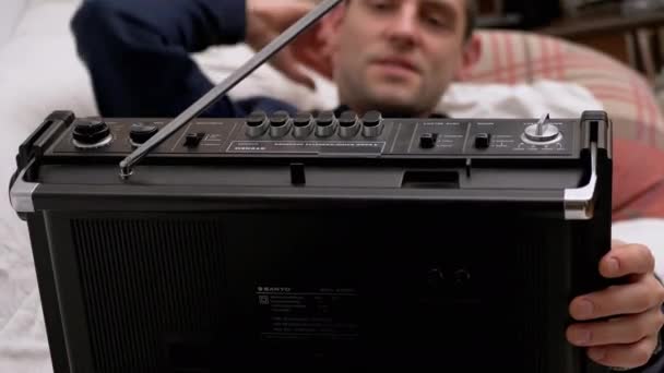 Müder Mann liegt auf Bett und drückt Play-Taste an altem Kassettenradio mit Antenne — Stockvideo