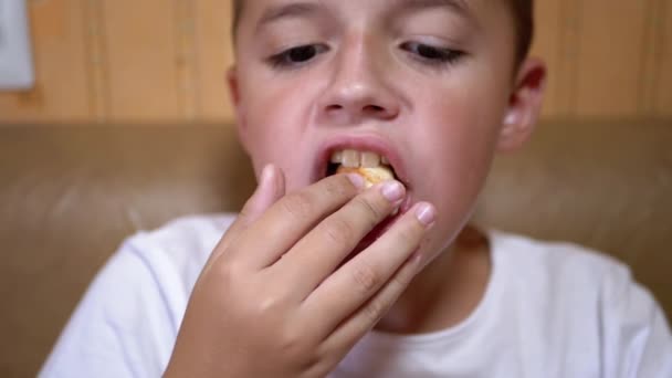 Голодный кавказский ребенок кладет чипсы в рот рукой. Мальчик ест фаст-фуд. — стоковое видео
