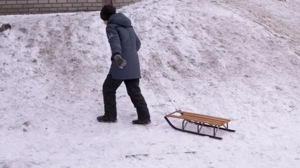 Szczęśliwy, zmęczony nastolatek z sankami wspinający się po Snowy Hill. Rudy policzek. — Wideo stockowe