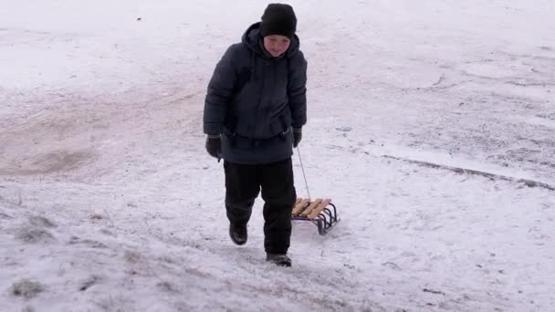 Szczęśliwy, zmęczony nastolatek z sankami wspinający się po Snowy Hill. Rudy policzek. — Wideo stockowe