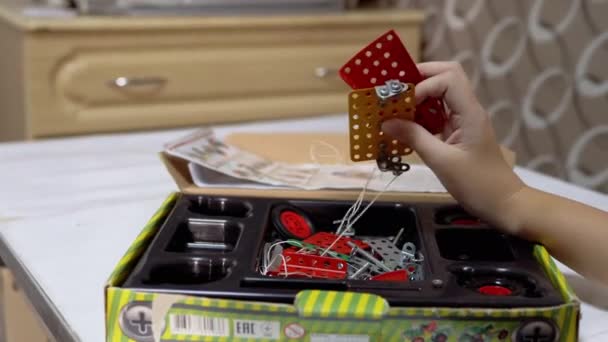Curious Boy juega con piezas de metal del constructor en la mesa en casa. 4K — Vídeo de stock