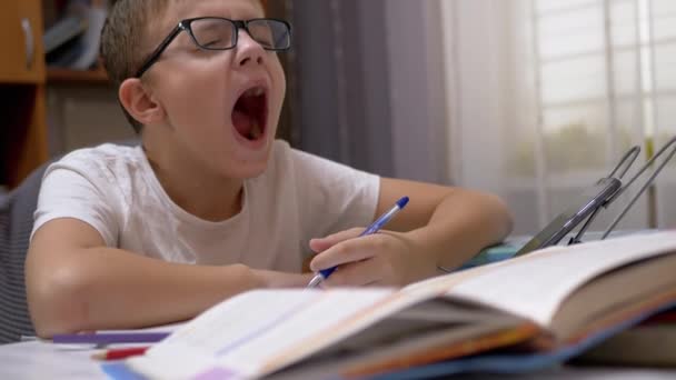 Müder Schuljunge mit Brille gähnt mit Stift in Notizbuch. 4K — Stockvideo