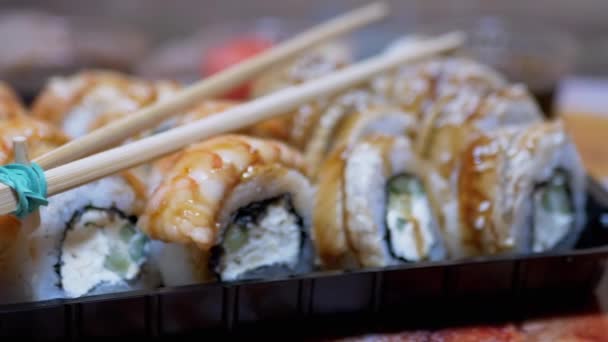 Японские суши в пластиковой коробке подаются на столе с бамбуковыми палочками. Zoom — стоковое видео