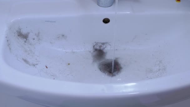 L'eau courante du robinet d'eau s'écoule dans un évier gorgé de cheveux, de laine, de déchets — Video