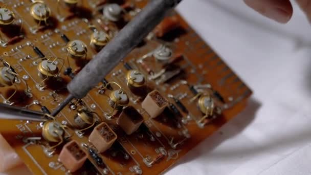 Человек распаивает транзисторы, радиодетали на электронной плате с паяльником — стоковое видео