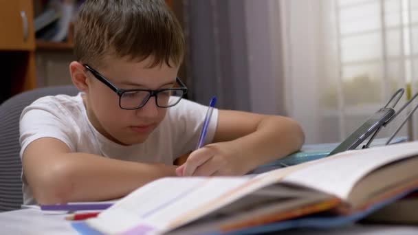 眼鏡をかけた神経質な学童は、ノートにペンで速く書きます。4K — ストック動画