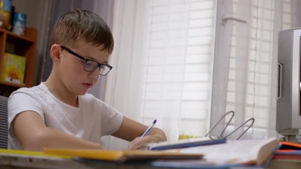 Serieuze schooljongen met bril Schrijft met pen in notitieboekje, doet lessen. 4K — Stockvideo