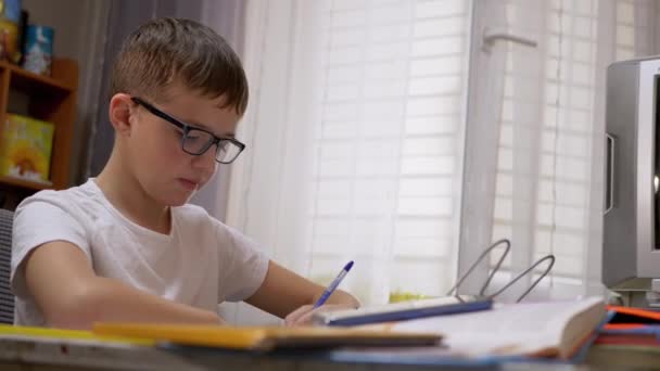 Školák v brýlích píše s perem v notebooku Má domácí úkol používat Smartphone — Stock video