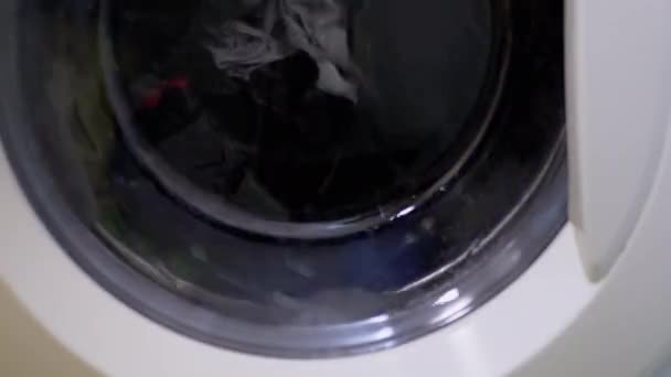 Стирка цветной одежды в бытовой стиральной машине. Вращающийся барабан. 4K — стоковое видео