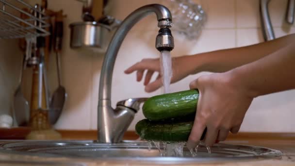 Mulher lavando pepinos verdes com água corrente de uma torneira em uma cozinha moderna — Vídeo de Stock