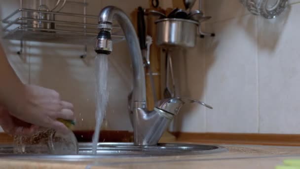 Vrouwelijke handen wassen gerechten in de keuken gootsteen onder stromend water. Tap lekt. 4K — Stockvideo