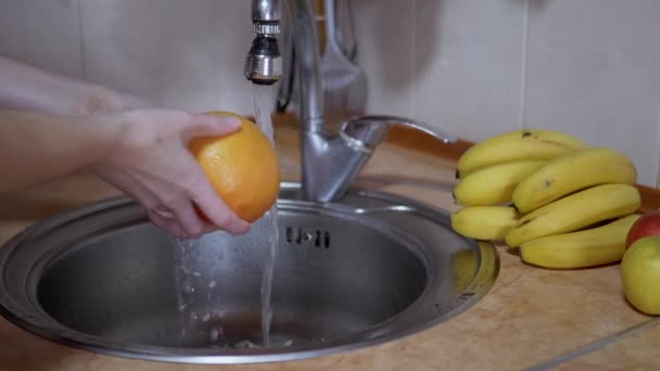 Mãos femininas lavando maçã, laranja, toranja, com água corrente da torneira — Vídeo de Stock