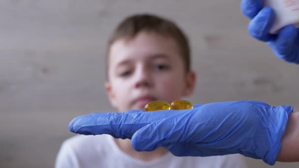 Doctor, un pediatra que usa guantes de nitrilo de látex, le da al niño dos pastillas. 4K — Vídeos de Stock