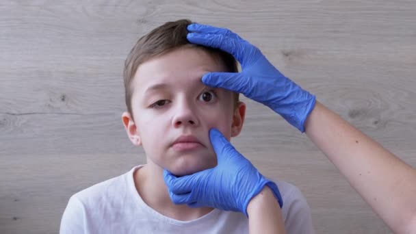 Педиатр в латексных нитрильных перчатках исследует глазное яблоко, зубы, рот мальчика. 4K — стоковое видео