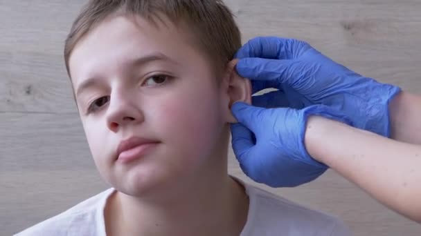 Доктор, ЛОР в латексных нитрильных перчатках исследует уши, аурикл мальчика-подростка — стоковое видео