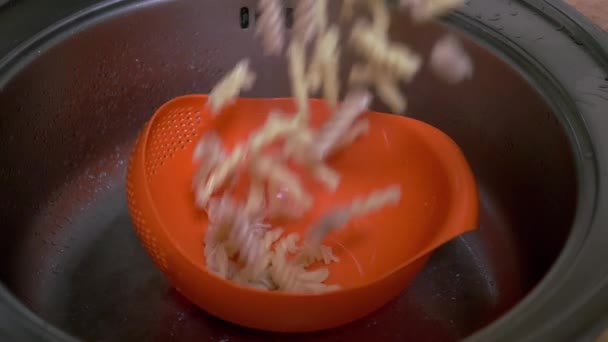 La hembra drena el agua de la pasta cocida en el colador de color naranja. Movimiento lento — Vídeos de Stock