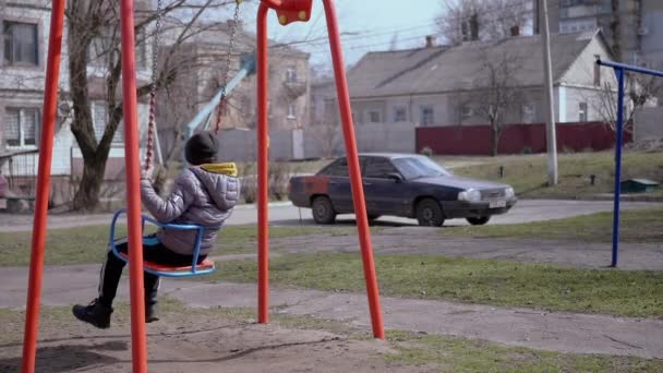 Vista lateral, solitario, triste niño balanceándose en un columpio en el patio sin amigos — Vídeos de Stock