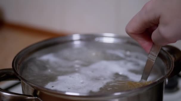 Mujer mano una cuchara agita la pasta, Macarrones en una cacerola de agua hirviendo — Vídeos de Stock