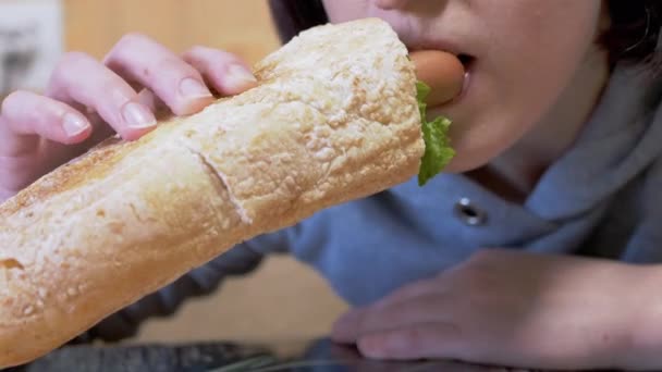 Głodna kobieta je apetycznego soczystego amerykańskiego hot doga z kiełbaskami w jadłodajni. 4K — Wideo stockowe