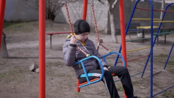 Magányos, szomorú gyerek, aki hintázik a barátok nélküli udvaron. Lassított mozgás — Stock videók