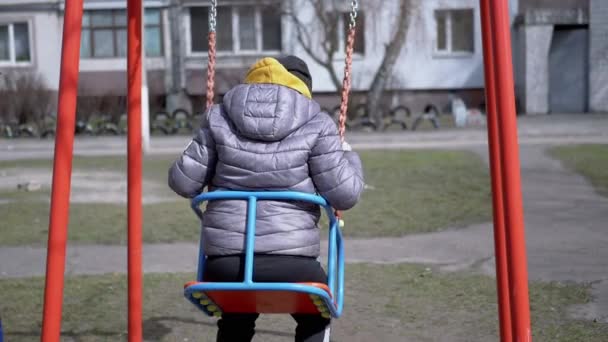 Achteraanzicht, eenzaam, verdrietig kind swingen op een schommel in de tuin zonder vrienden — Stockvideo