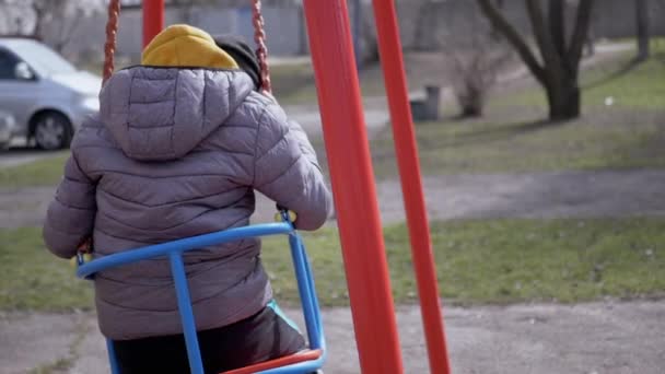 Visão traseira, solitária, criança triste balançando em um balanço no quintal sem amigos — Vídeo de Stock