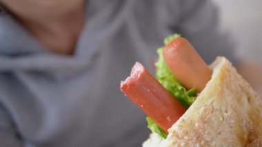 Lokantada sosisli, ısırılmış Amerikan sosisli sandviçi tutan kadın.