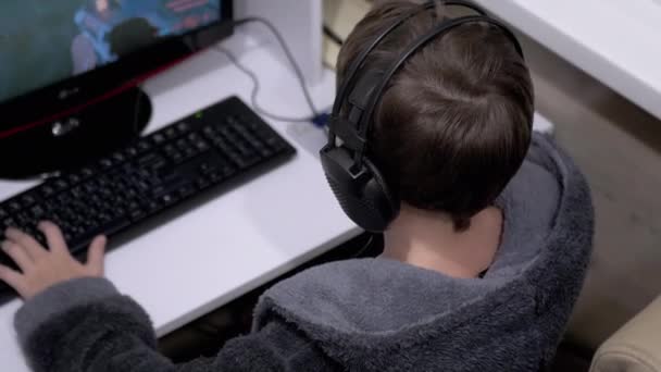 Nastoletni gracz w słuchawki, siedzieć w fotelu, Odtwarzanie gier wideo na komputerze — Wideo stockowe