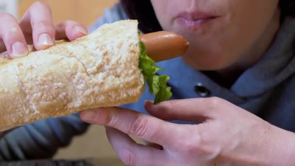 Éhes nő eszik étvágygerjesztő lédús amerikai hot dog kolbásszal étkezőben. Nagyítás — Stock videók