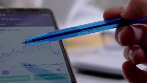 Бизнесмен касается экрана смартфона с ручкой, записывает данные в ноутбук — стоковое видео