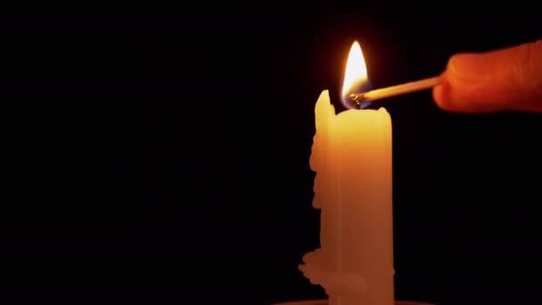 Женщина зажигает парафиновую свечу спичкой на черном фоне. 4K — стоковое видео