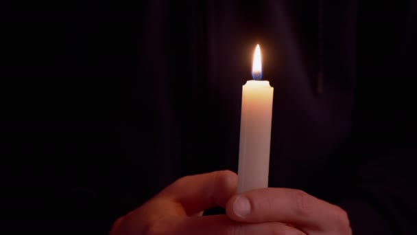 Homme tient dans les mains une bougie de cire éclairée dans une pièce sombre. 4K — Video