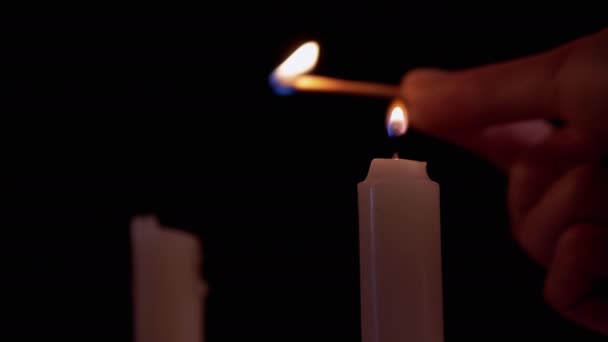 Две парафиновые свечи с помощью спички на черном фоне. 4K — стоковое видео