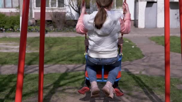 Vista trasera, solitario, niño triste balanceándose en un columpio en el patio sin amigos — Vídeo de stock